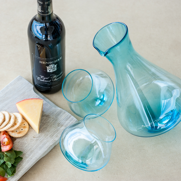 Blue glass decanter and wine glasses with a bottle of wine and appetizers on a table.