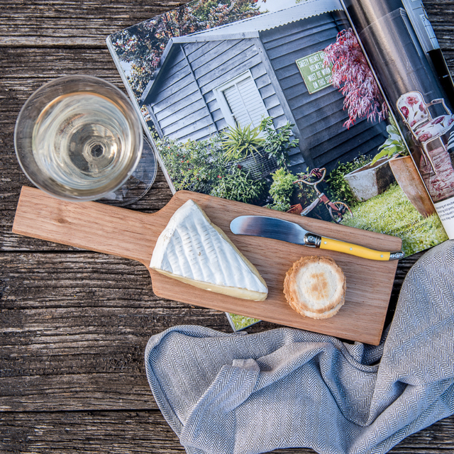 Wooden cheese board with a wedge of cheese and a small round bread on a rustic wooden surface.