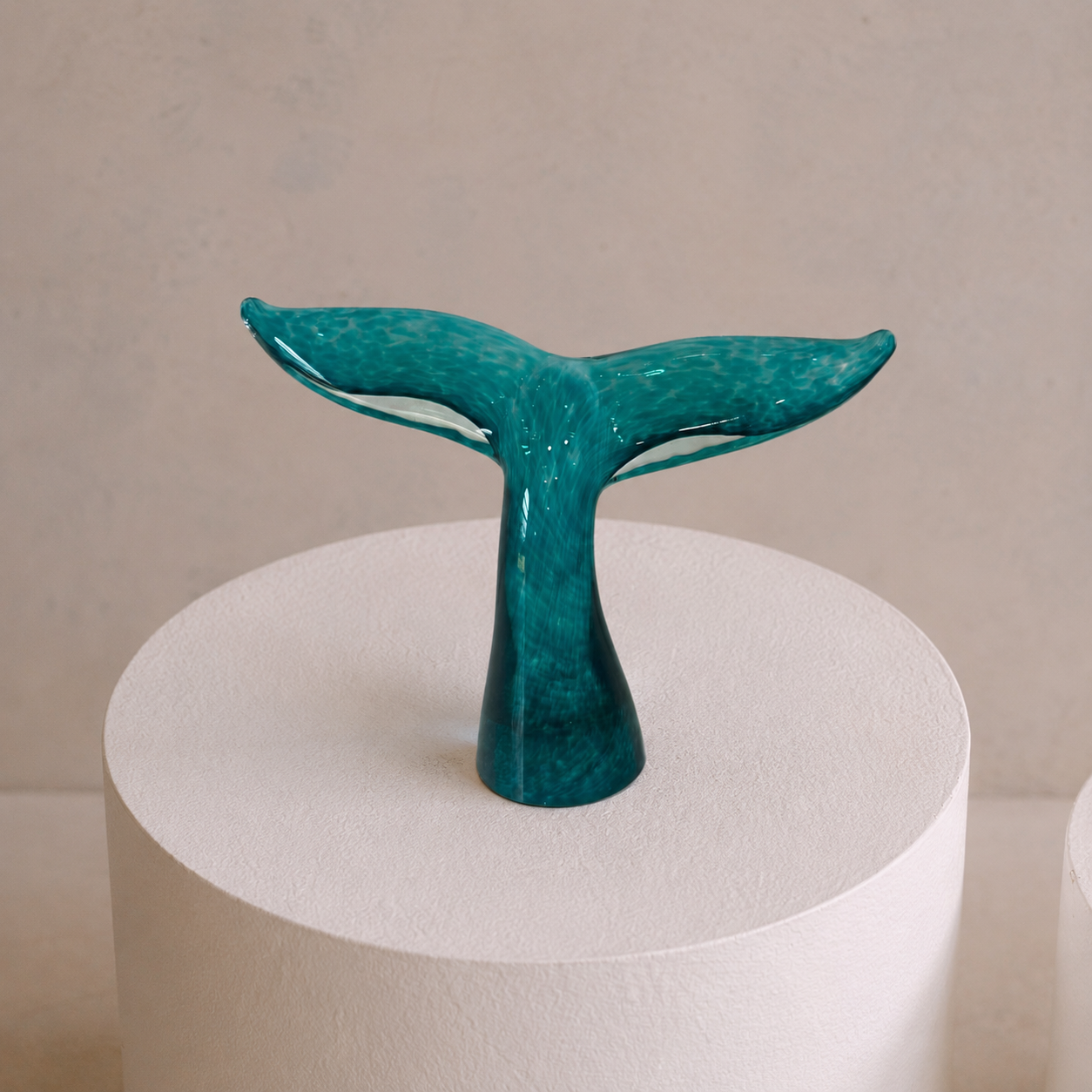 Handblown Whale Tail glass sculpture by South Australian artist Llewelyn Ash displayed on a white plinth with coastal styling.