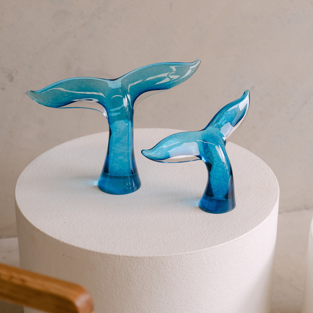 Handblown Whale Tail glass sculpture by South Australian artist Llewelyn Ash displayed on a white plinth with coastal styling.
