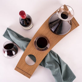 Overhead view of Emma Klau's handcrafted Australian oak Kinetic Wine Rack styled with a glass decanter, stemless wine glass, red wine bottle and sage green linen.