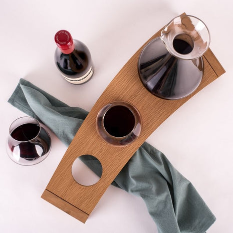 Overhead view of Emma Klau's handcrafted Australian oak Kinetic Wine Rack styled with a glass decanter, stemless wine glass, red wine bottle and sage green linen.