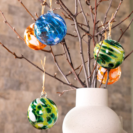Colourful handblown glass Christmas baubles by South Australian artist Nicole Ayliffe, displayed on branches in blue, green and orange.